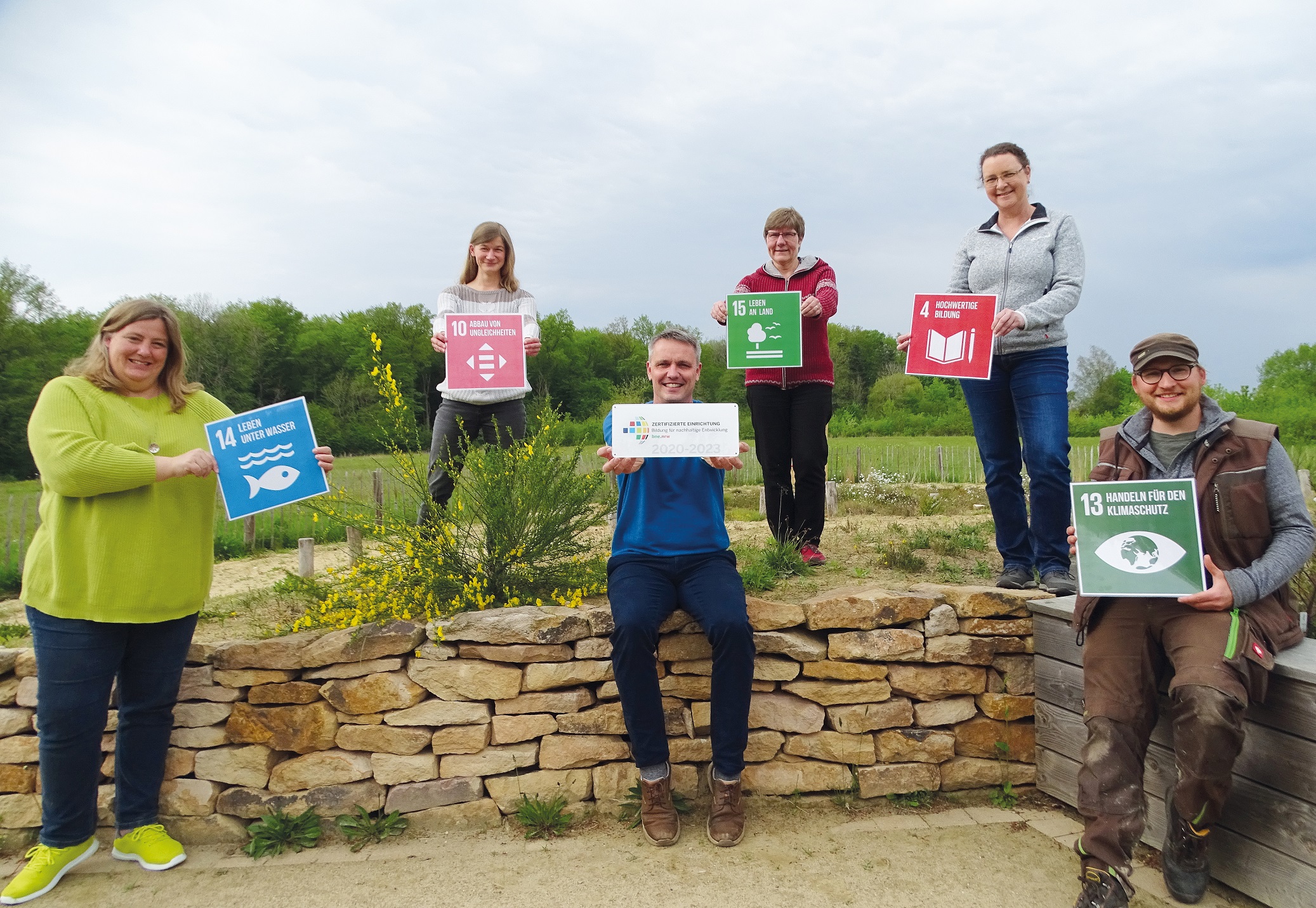 Gruppenfoto der Mitarbeiter:innen des NABU-Münsterland mit BNE-Türschild und SDGs