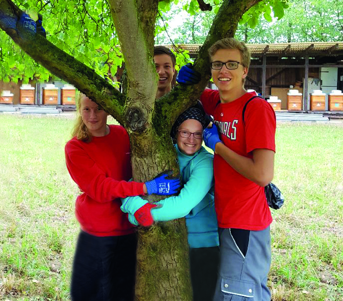 Vier junge Menschen umarmen einen Baum und lächeln in die Kamera.